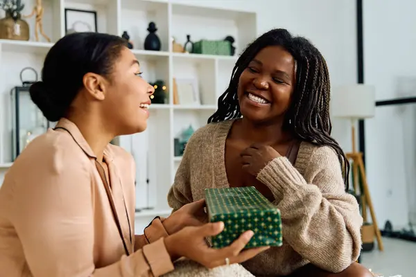 Dos mujeres comparten un momento sincero mientras intercambian regalos en un cálido espacio de vida. - foto de stock