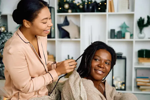 Due donne condividono il tempo gioioso insieme mentre intrecciano i capelli in uno spazio di vita splendidamente decorato. — Foto stock