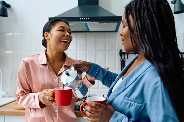 Two women share laughter and love while preparing coffee in their warm, inviting kitchen. — Stock Photo