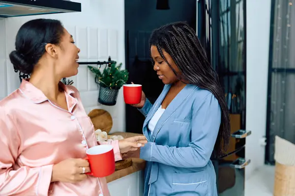 Dos mujeres comparten sonrisas y calidez en una cocina luminosa mientras disfrutan de bebidas calientes juntas. - foto de stock