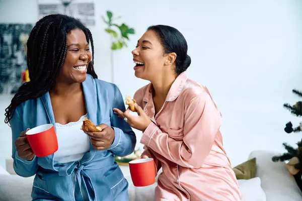 Two women laugh and enjoy their cozy morning together, sharing coffee and pastries. — Stock Photo