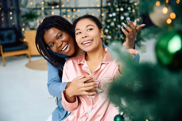 Due donne si abbracciano gioiosamente in uno spazio accogliente e decorato decorato con luci natalizie. — Foto stock