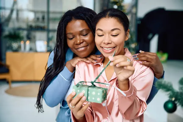Two women share a happy moment as they unwrap a beautifully wrapped gift in their home. — Stock Photo
