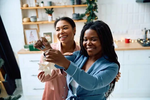 Zwei Frauen lächeln, als sie eine schöne Zierde aufhängen, die ihre Küche mit Urlaubsstimmung füllt. — Stockfoto