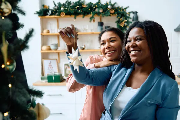 Two women happily decorate a Christmas tree with ornaments in a cozy, festive space. — Stock Photo