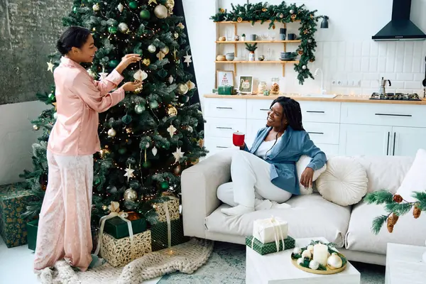 Two women happily decorate a festive Christmas tree while enjoying their time together indoors. — Stock Photo
