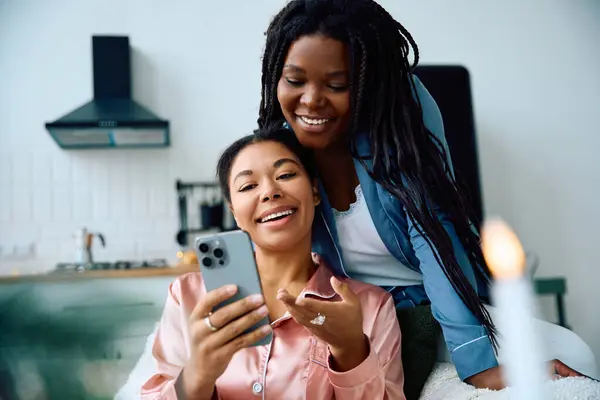 Two women enjoy each others company while looking at a phone in a bright, cozy living space. — Stock Photo