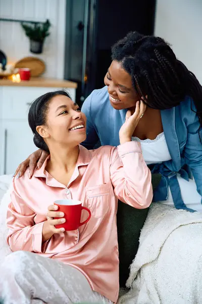 Two women relax in a warm living room, sharing laughter and warmth while enjoying drinks. — Stock Photo