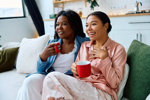 Two women relax together on a couch, enjoying warm drinks and heartfelt conversation. — Stock Photo