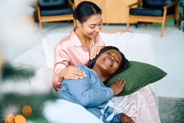 Two women enjoy a tender moment, cuddled on a sofa in a bright, inviting living space. — Stock Photo