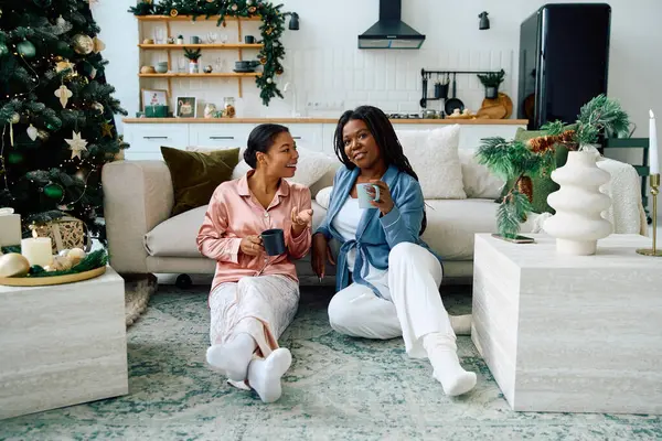 Two women relax on the floor, sharing laughter and warmth in their festive living room. — Stock Photo