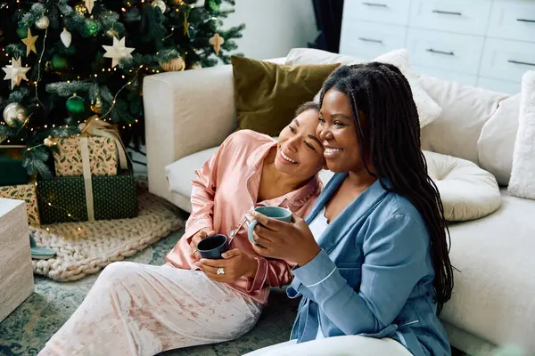 Two women embrace each other lovingly while enjoying warm drinks together at home. — Stock Photo