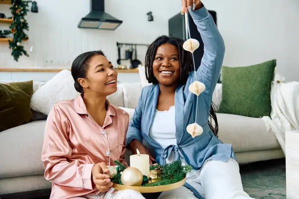Dos mujeres alegres comparten un momento de amor mientras decoran para la temporada navideña en casa. - foto de stock