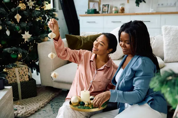 Dos mujeres elaboran alegremente decoraciones navideñas juntas en su acogedor hogar. - foto de stock