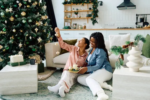 Two women share a festive moment together while enjoying a warm beverage and decorating a tree. — стоковое фото