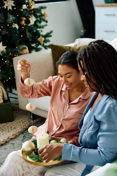 Dos mujeres comparten la risa mientras elaboran decoraciones festivas en casa durante las vacaciones. - foto de stock