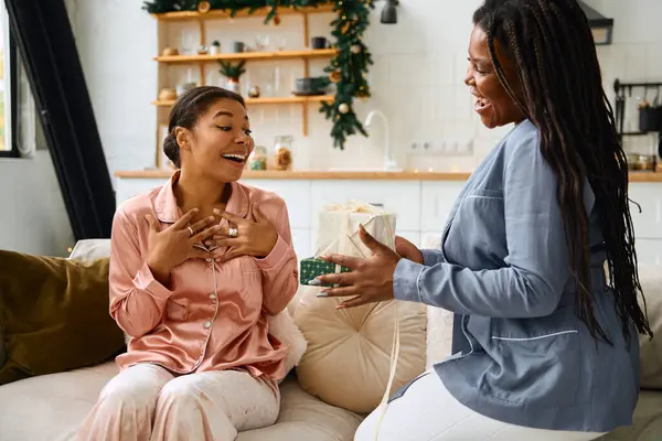 Two women share an intimate moment as one surprises the other with a thoughtful gift at home. — Stock Photo