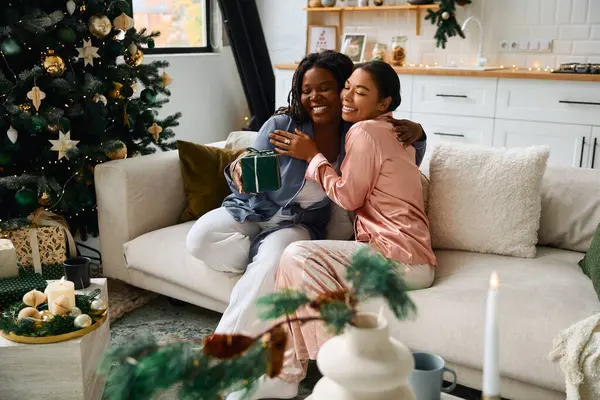 Dos mujeres se abrazan en un sofá, disfrutando de un ambiente festivo lleno de amor. - foto de stock