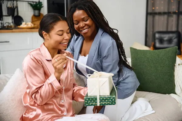 Two women share a delightful moment unwrapping a gift in a cozy setting at home. — Stock Photo