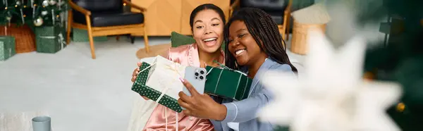 Two joyful women take a selfie while surrounded by festive decorations and gifts. — Stock Photo