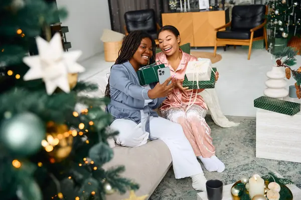 Two women exchange gifts and smiles in a cozy festively decorated space together. — Stock Photo