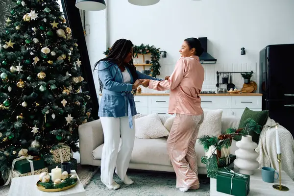 Two women dance together in festive attire, celebrating love and joy by the Christmas tree. — Stock Photo
