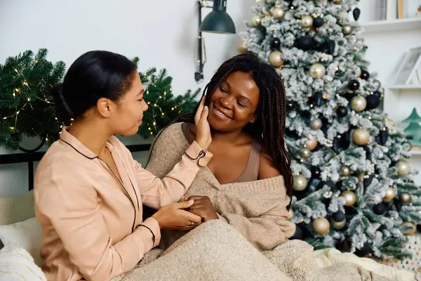Two women share a meaningful moment by a decorated Christmas tree, embracing their love joyfully. — Stock Photo