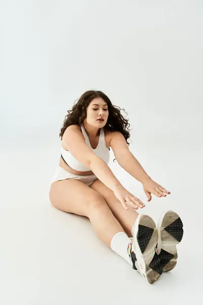 A young plus size woman stretches gracefully in trendy underwear, exuding confidence and beauty. — Stock Photo
