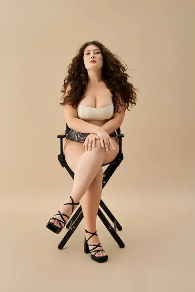 Junge Plus-Size-Frau präsentiert trendige Unterwäsche, während sie anmutig im Atelier sitzt. — Stockfoto