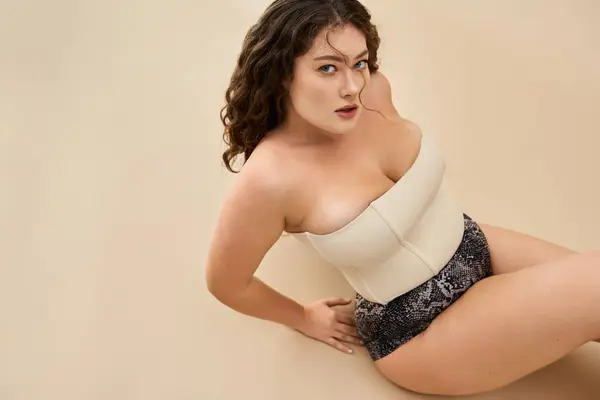 Plus size woman flaunts confidence and style in trendy lingerie on a neutral background. — Stock Photo