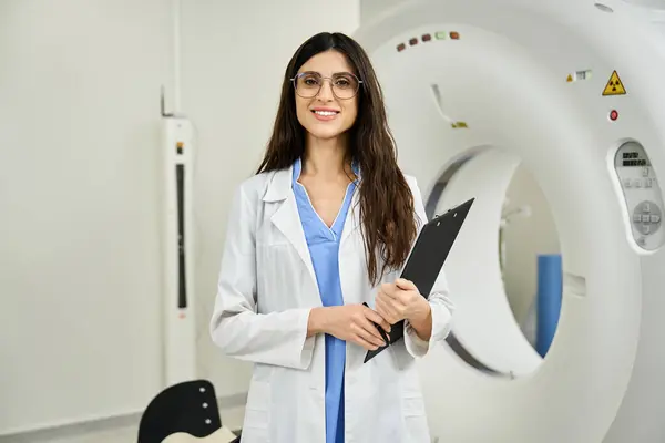 Attractive doctor with clipboard stands confidently beside MRI equipment in hospital. — Foto stock