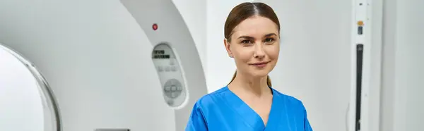 Attractive female doctor in blue scrubs stands confidently near MRI machine in hospital. — Stock Photo