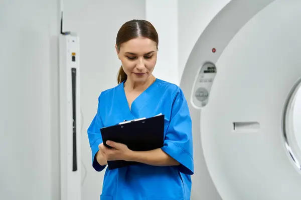 Attractive female doctor in scrubs meticulously reviews patient diagnostics in a radiology area. — Stock Photo