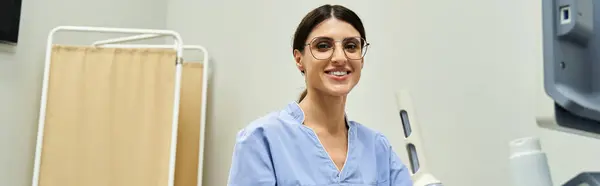 A skilled gynecologist in a blue scrubs smiles warmly in a contemporary clinic setting. — Stock Photo
