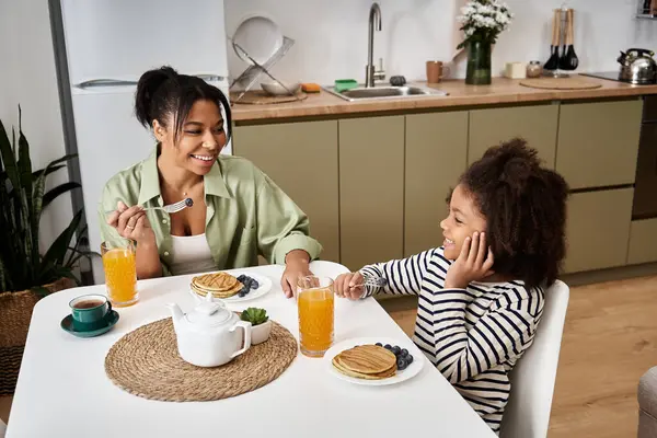A mother and her daughter enjoy a delightful breakfast with pancakes and juice at their home. — Stock Photo