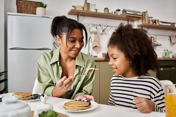Una madre serve con amore frittelle alla sua gioiosa figlia durante un'accogliente colazione a casa.. — Foto stock