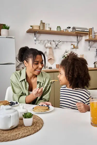 Una madre prepara frittelle mentre sua figlia attende con ansia di assaggiare il delizioso trattamento. — Foto stock