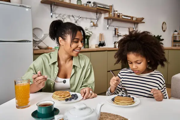 A mother and daughter joyfully share pancakes in their cozy kitchen. — Stock Photo