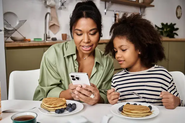 Mother and daughter share a special breakfast, enjoying pancakes and bonding over their devices. — Stock Photo