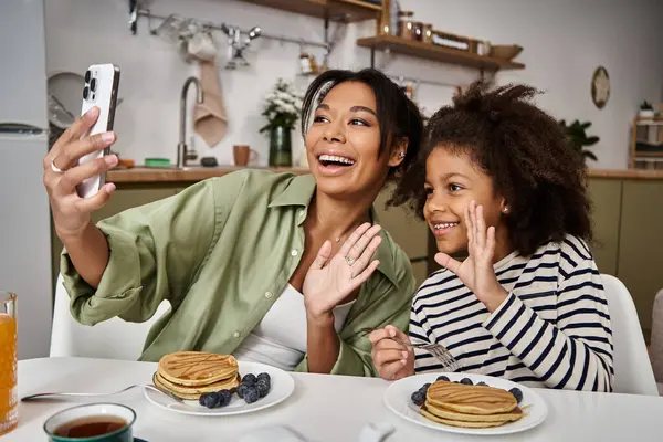 Mother and daughter share smiles while taking a selfie during breakfast filled with pancakes. — Stock Photo