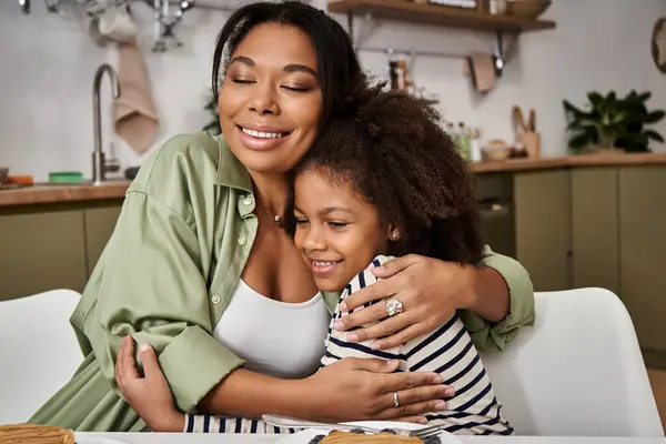 Une mère aimante embrasse chaudement sa fille sur une table de petit déjeuner remplie de joie. — Photo de stock