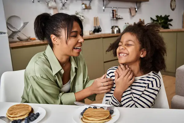 Two family members enjoy laughter and pancakes at breakfast in a cozy, modern kitchen setting. — Stock Photo