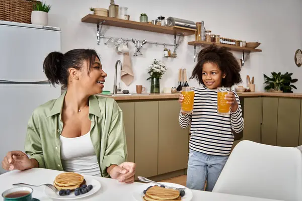 A loving mother smiles as her daughter brings drinks, creating joyful moments at breakfast. — Stock Photo