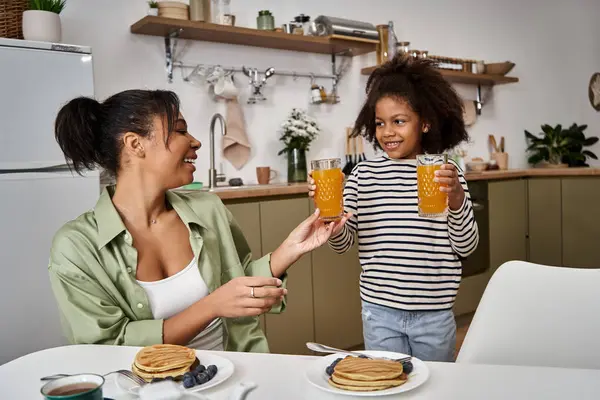 Mother and daughter celebrate their breakfast with pancakes and juice in a cheerful atmosphere. — Stock Photo