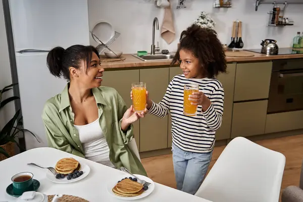 Mother and daughter celebrate a joyful breakfast, sharing smiles and fresh juices at home. — Stock Photo