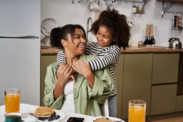 A mother enjoys playful affection from her daughter while sharing breakfast at home. — Stock Photo