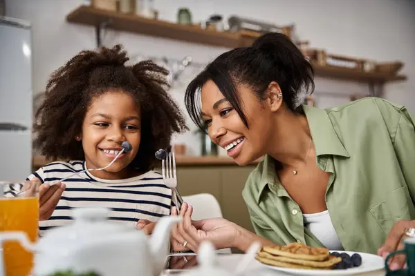 A mother and her little daughter share laughter while eating pancakes and fruit during breakfast. — Stock Photo