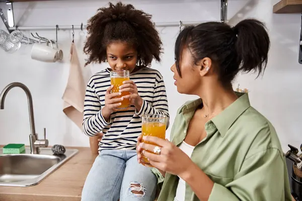 A mother and her daughter share joyful moments sipping vibrant drinks in their modern kitchen. — Stock Photo