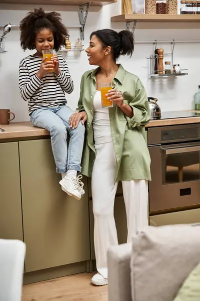 A woman and her young daughter happily sip refreshing beverages in a modern kitchen atmosphere. — Stock Photo