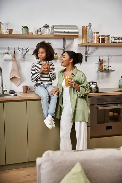 A mother and daughter enjoy refreshing drinks in their stylish kitchen. — Stock Photo